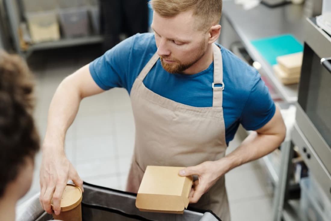 A restaurant kitchen staff member packing takeout food into delivery boxes