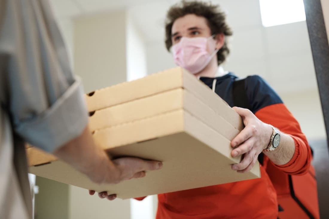 A delivery rider handing over pizza boxes at a customer's door