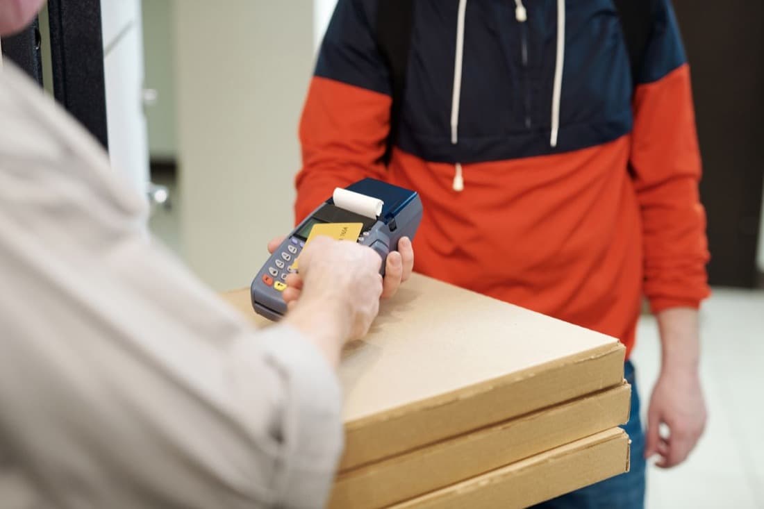 A delivery rider accepting card payment on a handheld POS device at a customer's doorstep