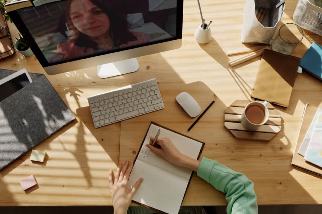 A person on a video call while taking notes at a desk