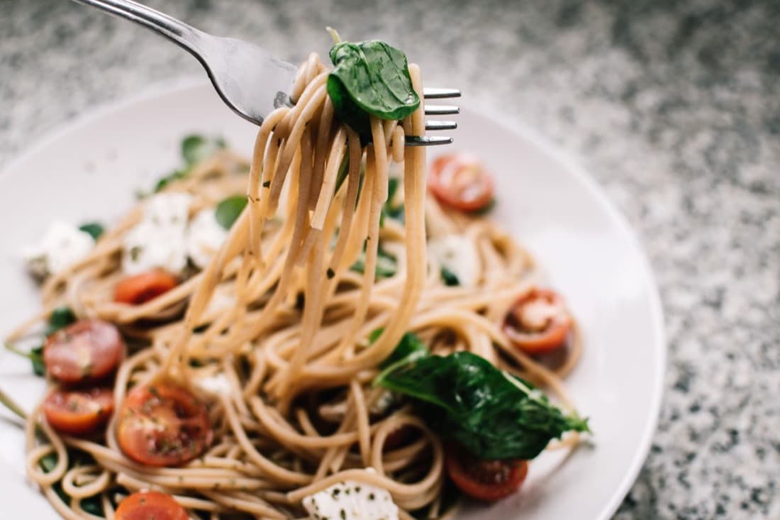 A close-up of a fork lifting spaghetti with fresh basil and cherry tomatoes from a plate