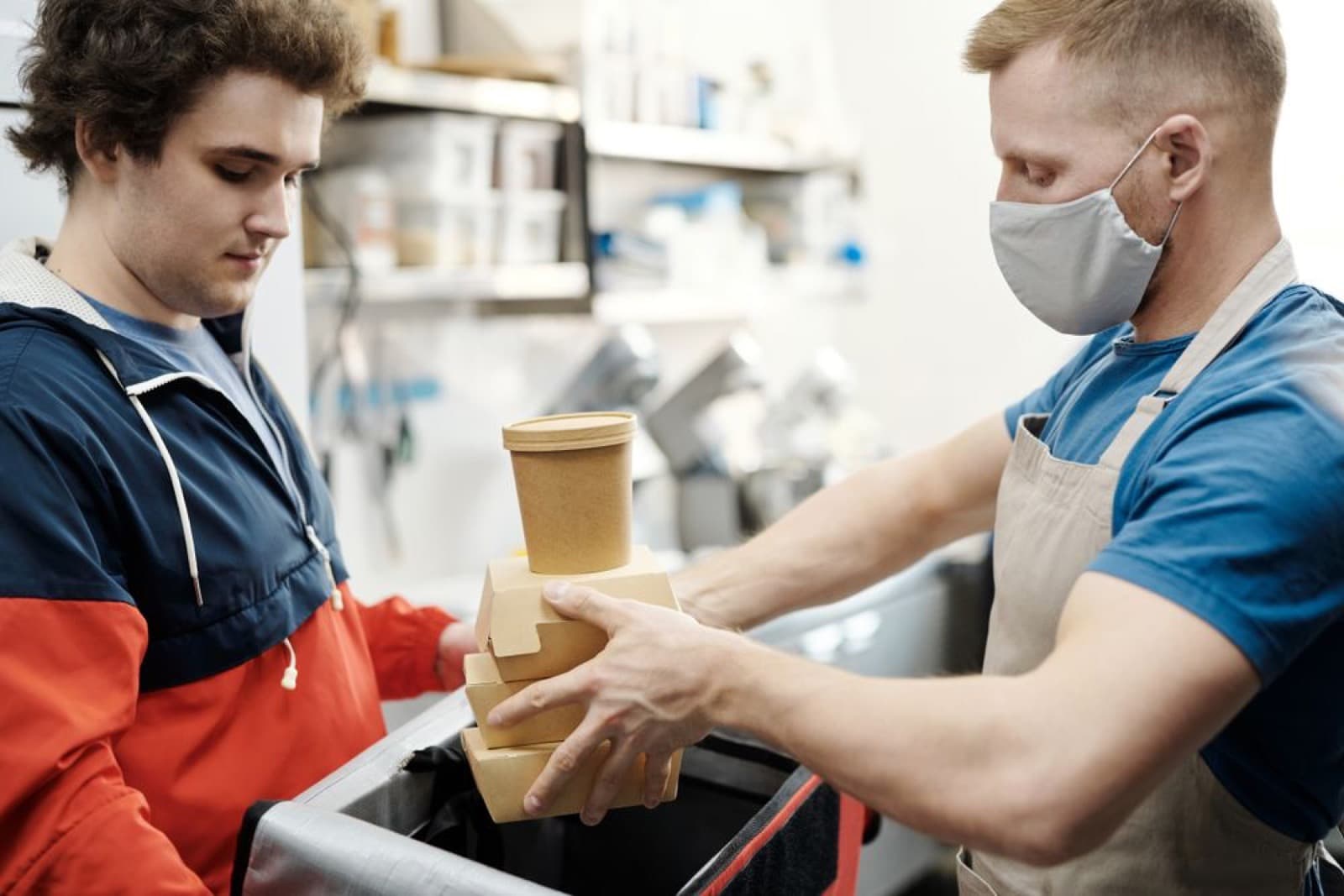 A restaurant worker handing packaged takeout containers to a delivery driver