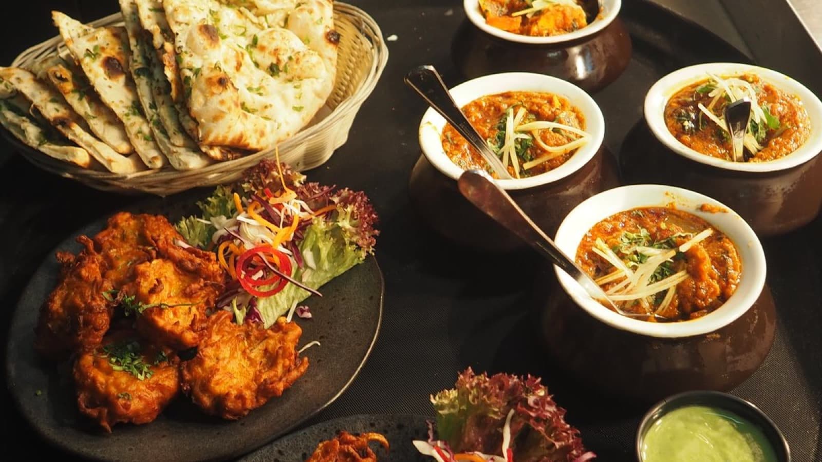 A spread of South Asian restaurant dishes — curries, naan, and pakoras — plated for delivery