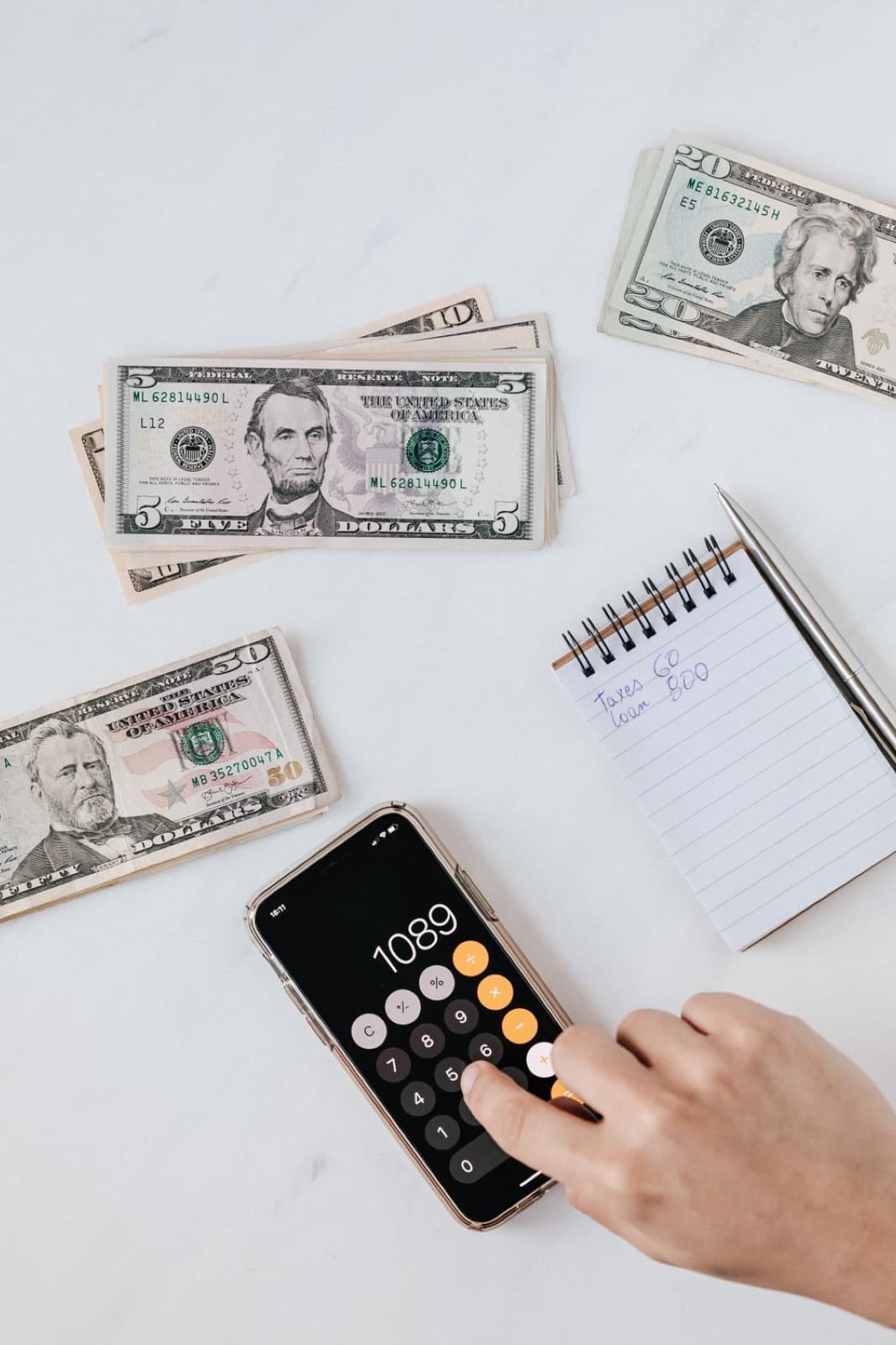 A calculator and cash on a table next to a handwritten budget notebook