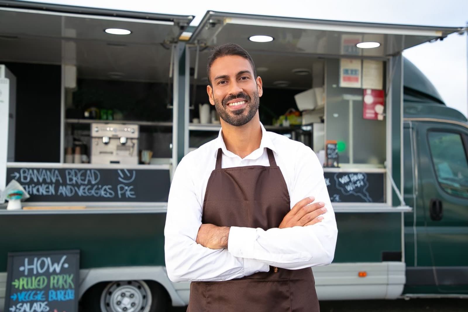 A smiling restaurant owner standing in front of his own branded food truck