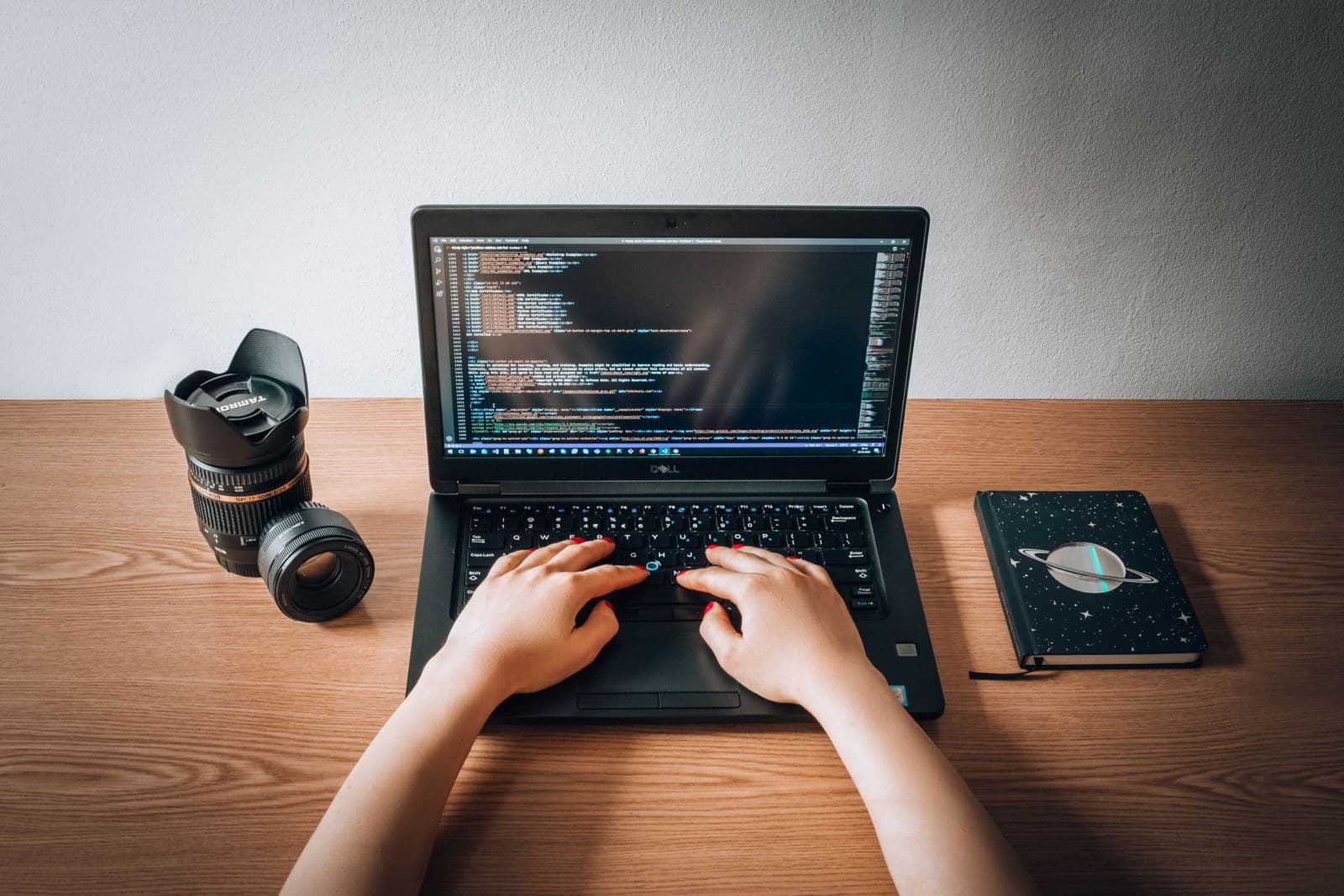 A person writing code on a laptop at a wooden desk