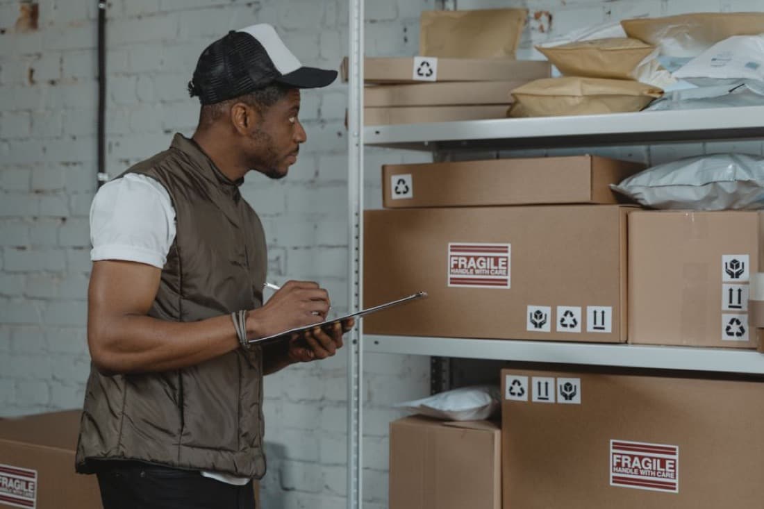 A staff member checking inventory boxes on warehouse shelving with a clipboard